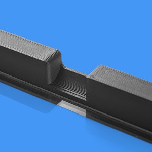 May include: A close-up of a black 3D printed object with a slot in the middle. The object has a textured surface.