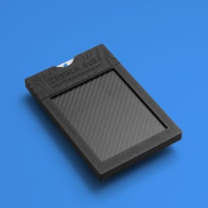 May include: A black rectangular Zebra 4x5 wet plate holder V2 with a textured frame and a central carbon fiber pattern insert. The device features a small cutout at the top edge revealing a glimpse of a white interior component.