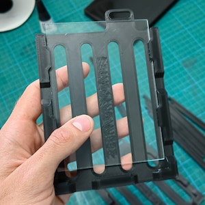 May include: A black plastic frame with a clear glass insert. The frame has four vertical slots and the text "REMARKABLE" is printed on the glass.