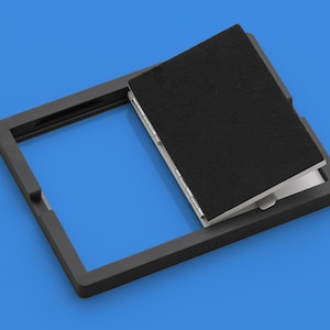 May include: A black frame with a black flap that opens to reveal a white interior. The frame is made of a textured material and has a raised edge. The flap is hinged and has a black fabric lining.