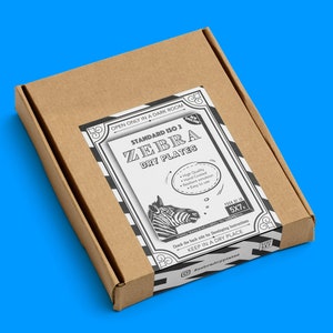 Puede incluir: Una caja de cartón marrón con una etiqueta en blanco y negro que dice "STANDARD ISO 2 ZEBRA DRY PLATES". La etiqueta también presenta una ilustración de cebra y el texto "OPEN ONLY IN A DARK ROOM" y "KEEP IN A DRY PLACE".