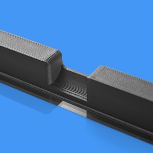 Peut inclure: Gros plan sur un objet noir imprim&eacute; en 3D avec une fente au milieu. L'objet est en plastique et a une surface textur&eacute;e.