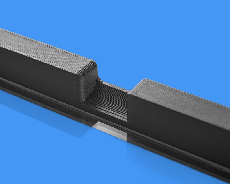 Peut inclure: Gros plan sur un objet noir imprim&eacute; en 3D avec une fente au milieu. L'objet est en plastique et a une surface textur&eacute;e.