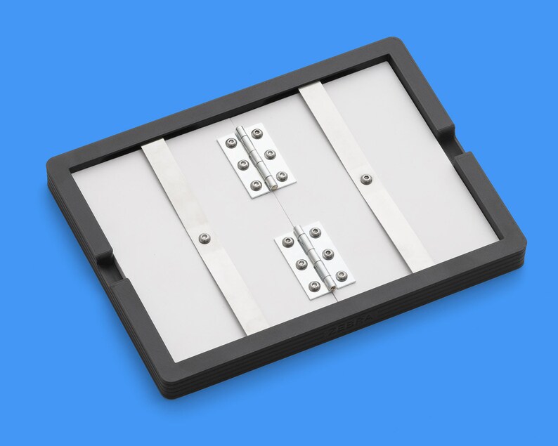 May include: A black framed folding board with two sets of silver hinges. The board is made of a light gray material and has a black rubber border.