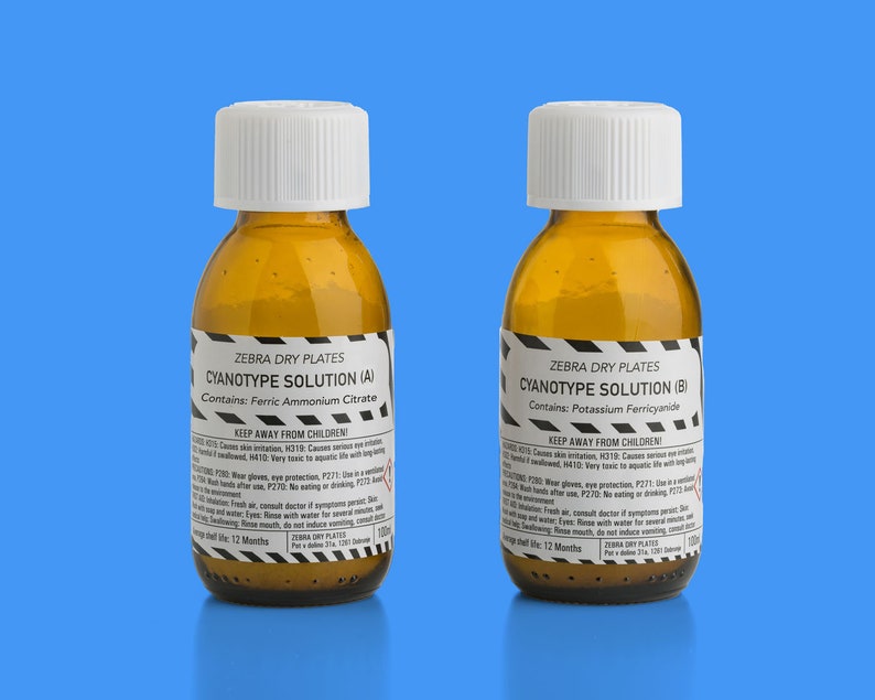 May include: Two amber glass bottles with white lids labelled "Zebra Dry Plates Cyanotype Solution (A) Contains: Ferric Ammonium Citrate" and "Zebra Dry Plates Cyanotype Solution (B) Contains: Potassium Ferricyanide". Both bottles have black and yellow warning labels and say "Keep Away From Children".