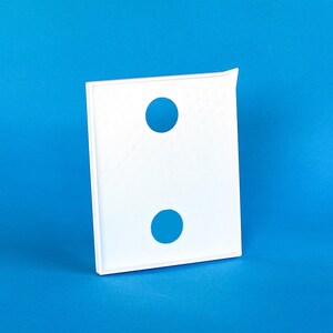 May include: A white, rectangular object with two blue circular cutouts. The object has a thin, raised border and a small, curved extension on one corner. The background is a solid, bright blue.