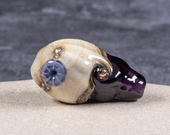 Cuenta de vidrio soplado hecha a mano con conchas marinas en color morado oscuro transparente y marfil.