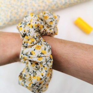 K&ouml;nnte beinhalten: Ein wei&szlig;er und gelber Haargummi mit Blumenmuster.
