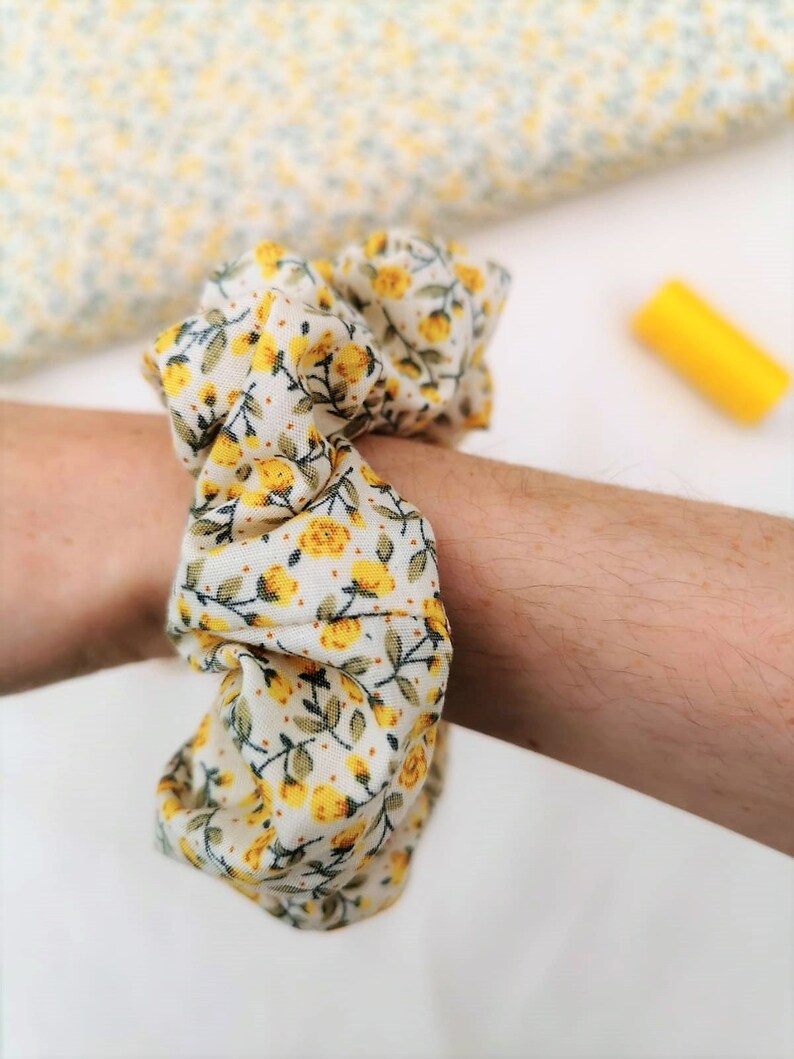 K&ouml;nnte beinhalten: Ein wei&szlig;er und gelber Haargummi mit Blumenmuster.
