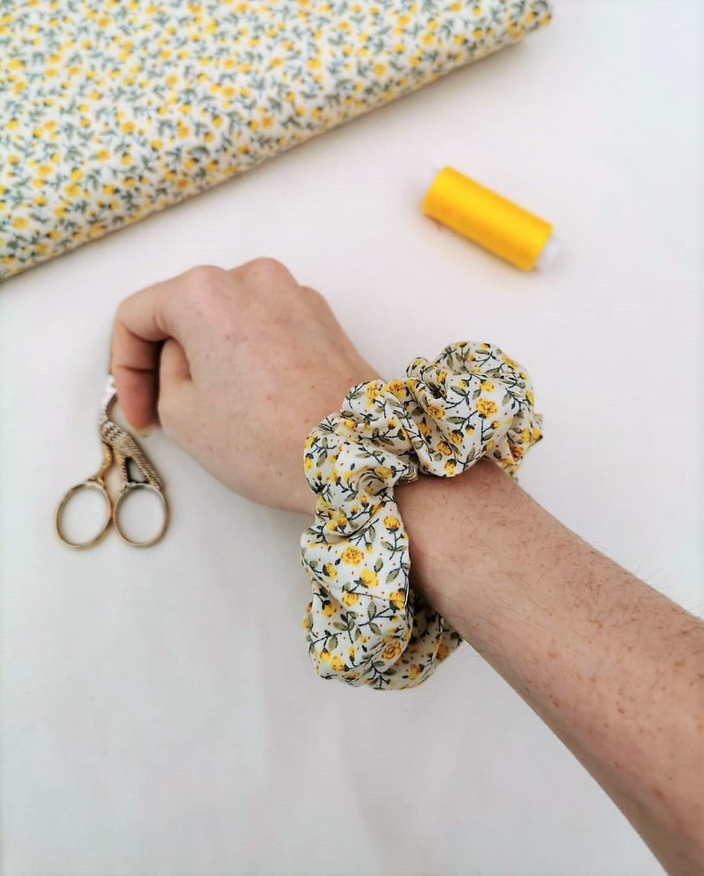 K&ouml;nnte beinhalten: Ein wei&szlig;er und gelber Blumenmuster-Haargummi mit gerafftem Stoffdesign.