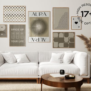 Puede incluir: Un interior de sala de estar con un sofá blanco y una mesa de centro. La pared detrás del sofá está decorada con una pared de galería de impresiones enmarcadas en varios estilos y colores. Las impresiones incluyen patrones geométricos, diseños abstractos y arte basado en texto. La habitación está decorada con un jarrón de hierba de la pampa seca y una lámpara de pie.