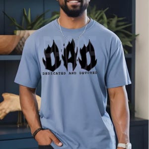 May include: A light blue t-shirt with a black graphic of the word "DAD" in flames. The text "DEDICATED AND DEVOTED" is printed below the graphic.