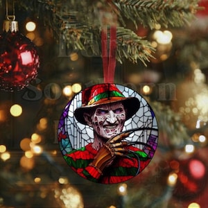 May include: A round Christmas ornament featuring a stained glass style image of Freddy Krueger from the Nightmare on Elm Street horror film series. He is wearing a red and green striped sweater and a brown hat with a green brim. He has a menacing expression and is holding a glove with razor-sharp blades.