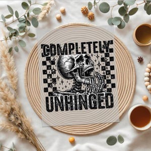 May include: A black and white graphic print on a square card. The design features a detailed illustration of a skeleton with the words "COMPLETELY UNHINGED" in bold, distressed font. The background has a checkered pattern.