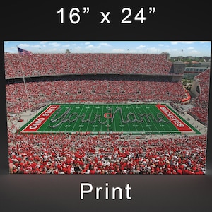 May include: A print of a football stadium with a large crowd of people wearing red. The Ohio State marching band is forming the words "Ohio State" on the field. The words "Buckeyes" are also visible on the field.