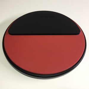 May include: A red and black practice drum pad with the text "Revolution" printed on the black portion. The pad is circular and has a black rim.