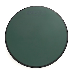 May include: A dark green, circular drum practice pad with a black rim. The text "okeecajon" and "handmade in istanbul" are printed on the surface. The pad is designed for percussion practice.