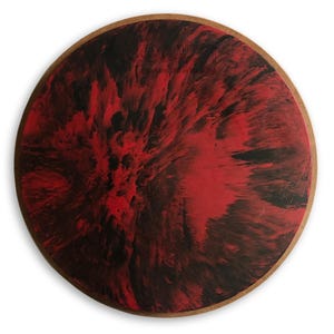 May include: Round wooden coaster with a red and black abstract design. The design resembles a swirling, marbled effect.