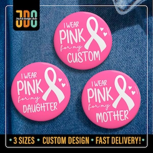 May include: Three pink buttons with white text and a white ribbon design. The buttons read "I wear pink for my custom", "I wear pink for my daughter", and "I wear pink for my mother". The buttons are on a blue denim background.