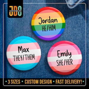 May include: Three circular badges with names and pronouns. One features a rainbow design with "Jordan HE/HIM". Another has a light blue and white design with "Max THEY/THEM". The third has a pink and white design with "Emily SHE/HER".