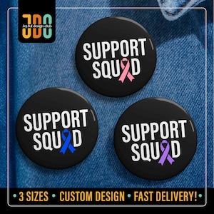 May include: Three black circular badges with the text "SUPPORT SQUAD" in white. Each badge features a different coloured ribbon: pink, blue, and purple. The badges are on a denim background.
