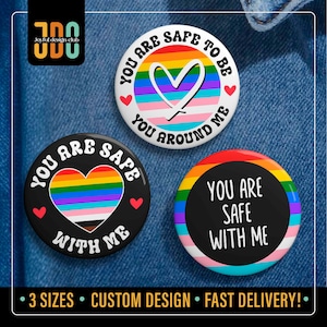 Puede incluir: Tres botones redondos con los textos "You Are Safe" y "You Are Safe With Me". Los botones presentan diseños de corazón y círculo arcoíris, con texto blanco. Sobre un fondo de mezclilla azul.