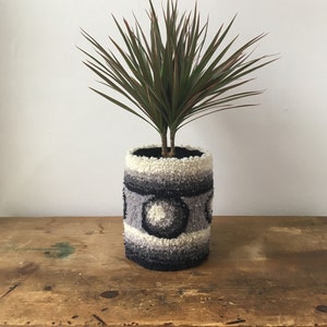 May include: A potted plant with green leaves in a grey and white patterned planter with black circles.