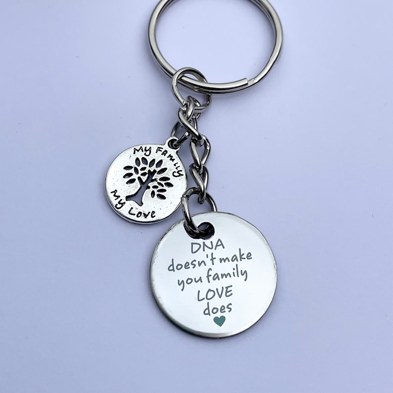 May include: Silver keychain with two round charms. The larger charm has the text "DNA doesn't make you family LOVE does" with a small green heart. The smaller charm has a tree with the text "My Family My Love".