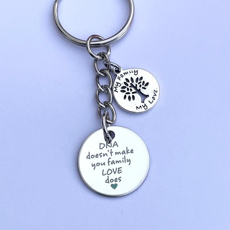 May include: Silver keychain with two charms. The larger charm has the text "DNA doesn't make you family LOVE does" with a small green heart. The smaller charm has a tree with the text "My Family My Love".