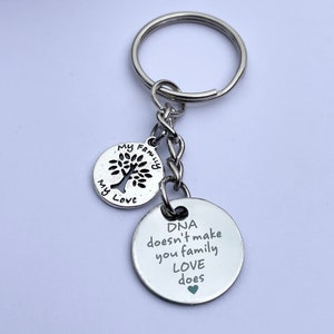 May include: Silver keychain with two round charms. The larger charm has the text "DNA doesn't make you family, LOVE does" with a small heart at the end. The smaller charm has a tree with the text "My Family My Love".