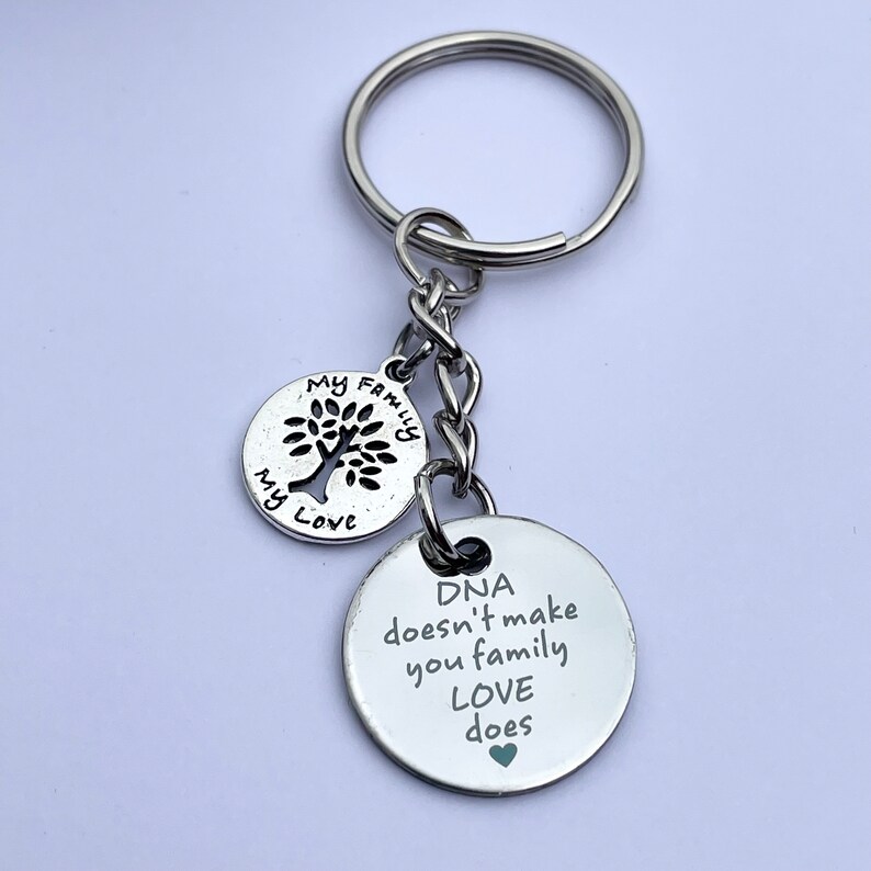 May include: Silver keychain with two round charms. The larger charm has the text "DNA doesn't make you family, LOVE does" with a small heart at the end. The smaller charm has a tree with the text "My Family My Love".