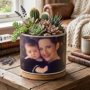 May include: A round planter with a photograph of a mother and child, planted with a selection of succulents and cacti. The planter has a wooden base. The arrangement includes green, pink, and purple plants.