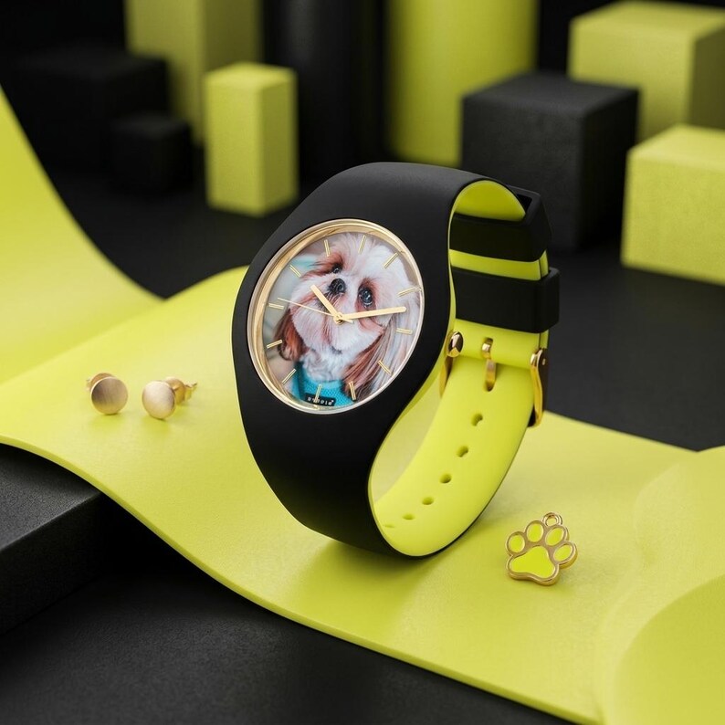 May include: Black and yellow wristwatch with a dog face on the watch face. The watch has a black band with a yellow underside. Gold stud earrings and a paw print charm are also present.