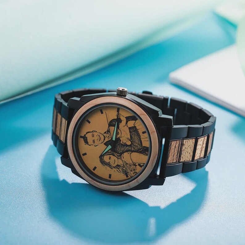 Op de afbeelding: Een gepersonaliseerd houten horloge met een zwarte en goudkleurige wijzerplaat en band. De wijzerplaat van het horloge heeft een laserge&euml;tste afbeelding van een stel. Het horloge heeft een zwarte bezel en een combinatie van zwarte en houten schakels.