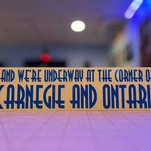 May include: A yellow sign with blue text that reads "And we're underway at the corner of Carnegie and Ontario."