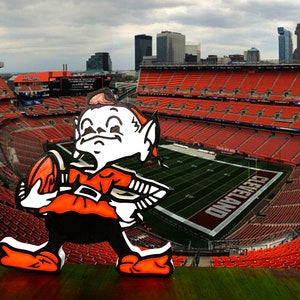 May include: A cartoon elf mascot holding a football in front of a large stadium with orange seats. The stadium is called "CLEVELAND".