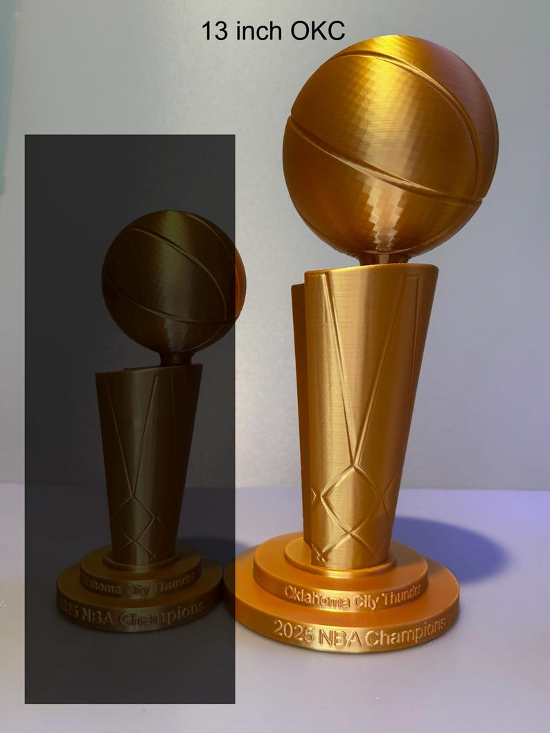 May include: A gold-coloured 33 cm Oklahoma City Thunder 2025 NBA Champions trophy featuring a basketball mounted on a tapered base. The base is engraved with the text Oklahoma City Thunder 2025 NBA Champions. Two versions are shown.