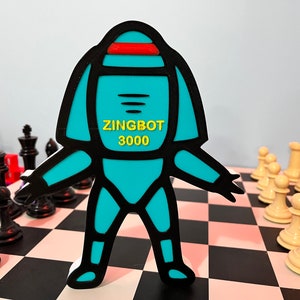 May include: A turquoise blue robot figurine with black outlines and a red stripe on its head. The robot is standing on a black and white checkered chessboard. The robot has the text "ZINGBOT 3000" printed on its chest.