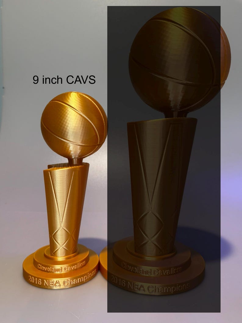 May include: Two gold-coloured 3D printed trophies featuring a basketball atop a tapered base. The base is inscribed with "Cleveland Cavaliers 2016 NBA Champions". The smaller trophy is labelled "9 inch CAVS" in black text above it.