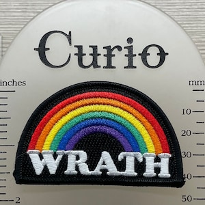 May include: A black and white embroidered patch with a rainbow arc and the word "WRATH" in white letters. The patch is approximately 2 inches wide.