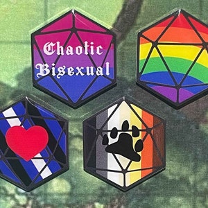 May include: Four different colored dice with black outlines and various symbols and text. The dice are all in the shape of a d20. The first die is purple and blue with the text "Chaotic Bisexual". The second die is rainbow colored. The third die is blue, black, and white with a red heart. The fourth die is black, white, orange, and yellow with a black paw print.
