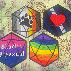 May include: Four embroidered patches shaped like a 20-sided die, each with a different design. The first patch is gray, white, and orange with a paw print. The second patch is blue, white, and black with a red heart. The third patch is pink, blue, and purple with the text "Chaotic Bisexual". The fourth patch is rainbow colored.