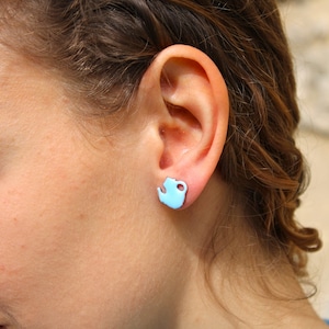 May include: A close-up of a person's ear with a light blue teapot-shaped stud earring.