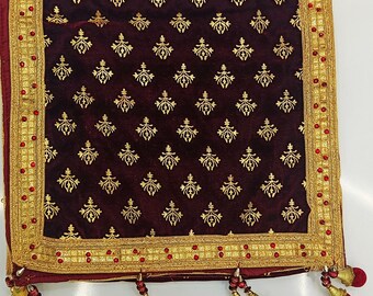 May include: A burgundy velvet textile with a repeating gold floral pattern. The edges are trimmed with gold embroidery, red beads, and burgundy tassels. The textile is likely a shawl or decorative cloth.