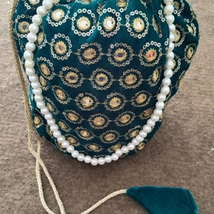 May include: A green velvet drawstring bag with gold embroidery and a pearl necklace. The bag has a long drawstring and two tassels.