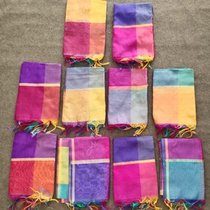 Può includere: Una collezione di sciarpe colorate e trasparenti. Ogni sciarpa è rettangolare con un design a blocchi bicolore, con sfumature di rosa, viola, giallo e blu. I bordi sono rifiniti con una frangia di filo coordinato.