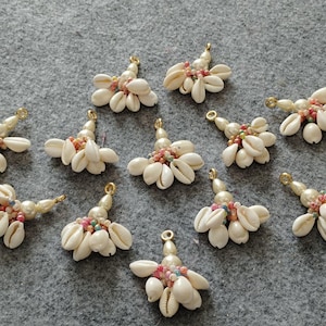 May include: Twelve white shell charms with gold accents and colourful beads. Each charm is shaped like a triangle with the shells arranged in a fan shape.