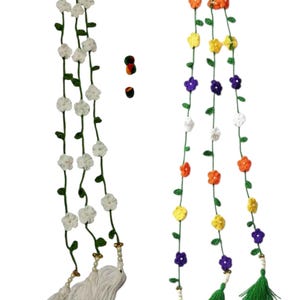 May include: Two long, vertical crochet garlands featuring green vines with small leaves. The left garland has white flowers and white tassels. The right garland has multi-colored flowers in orange, yellow, purple, and white, with green tassels.