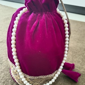 May include: A deep purple velvet drawstring bag with a white pearl necklace wrapped around it. The bag has gold embroidery around the top.