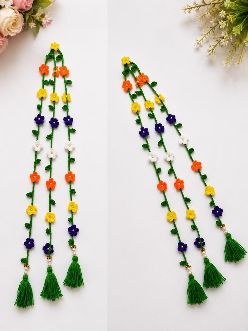 May include: Three long, green crocheted vine strands decorated with small, multi-colored flowers in yellow, orange, white, and purple. Each vine features tiny green leaves and ends in a green yarn tassel accented with small white and gold beads.